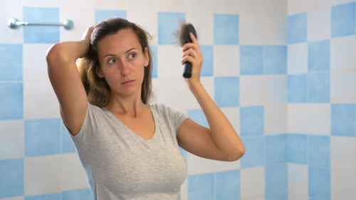 Woman Looking at Mirror, Brushing Hair. Irritated Young Girl Dissatisfied with Damaged Dry Hair