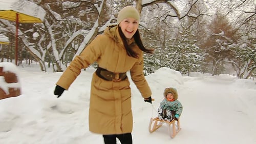 Woman Pulling Child on Sled in Snowy Park