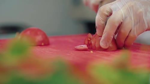 Gloved Hands Slice Red Tomato on Cutting Board
