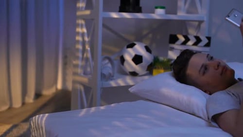 Teenager Lies on Bed Looking at Mobile Phone