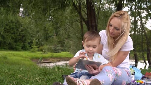 Happy Mother and Her Little Son Enjoying Playing on Tablet Computer in the Park
