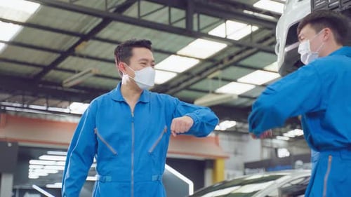 Deux mécaniciens automobiles asiatiques portent un masque et touchent le coude.