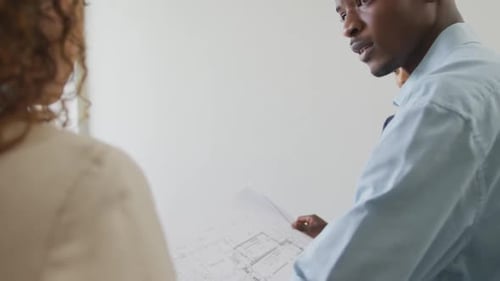 Biracial male and female architects checking architects plans in modern office