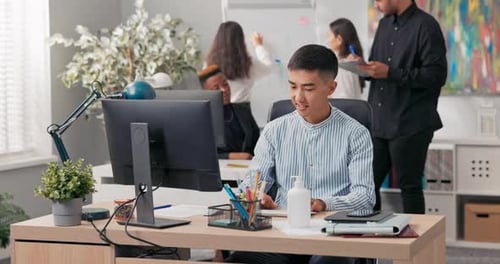 A Man of Asian Korean Beauty Sits in Front of an Office Computer Using a Web Browser Working in