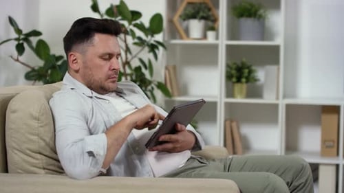 Man Relaxes on Sofa Using Tablet Device