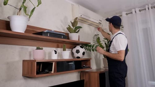 Male Handyman in Overalls Repairs or Cleans the Air Conditioner in the Apartment