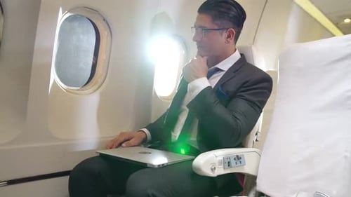 Man in Suit Contemplates on Airplane With Laptop