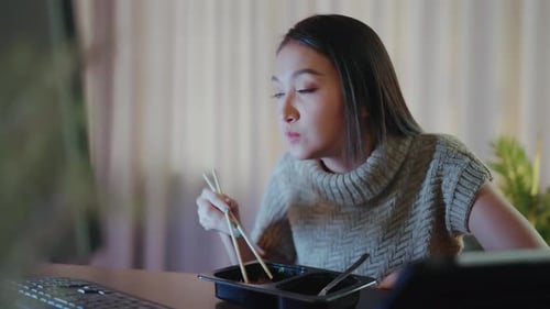 Young Woman Eating Takeout While Working on Computer