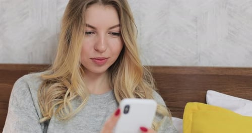 Caucasian Woman Laying on Her Bed Scrolling Over and Chatting on Smartphone