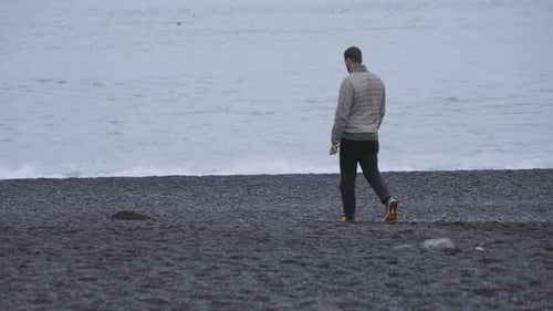 Breathtaking View of Man Strolling on the Reynisfjara Black Sand BeachIceland
