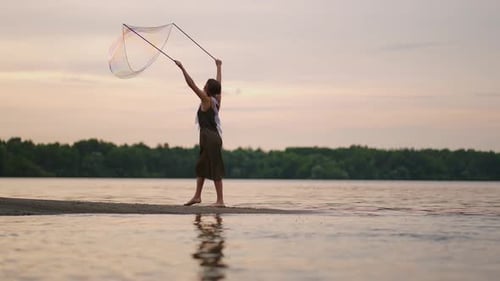 A Young Female Artist Shows a Soap Bubble Show Blowing Up Huge Soap Bubbles on the Shore of a Lake