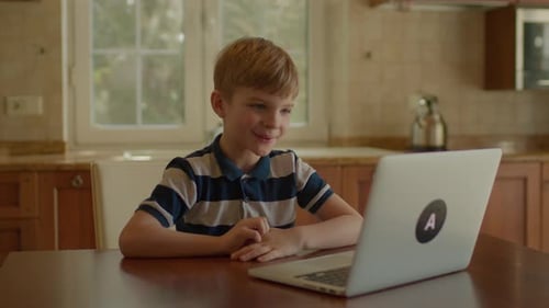 School Boy Learning Online Using Laptop Sitting in the Kitchen at Home