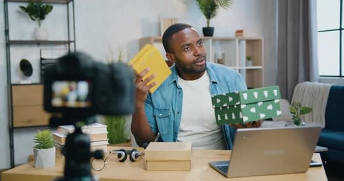 Chico afroamericano que sostiene cajas de cartón con regalos en la mano durante la grabación de un vlog
