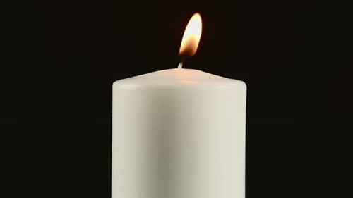 A Burning White Candle on a Black Background or in the Dark