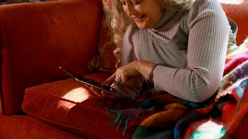 Woman Smiling, Using Tablet on Couch at Home