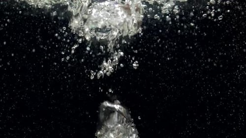 Luftblasen in Zeitlupe im Wasser, die auf schwarzem Hintergrund an die Oberfläche steigen