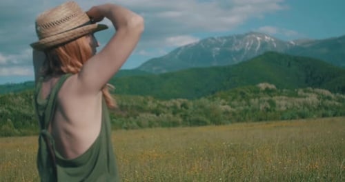 Femme avec chapeau regardant vers les montagnes