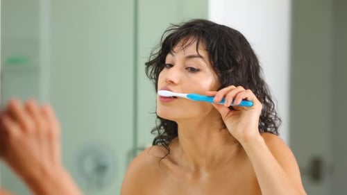Woman Brushing Teeth in a Bright Bathroom