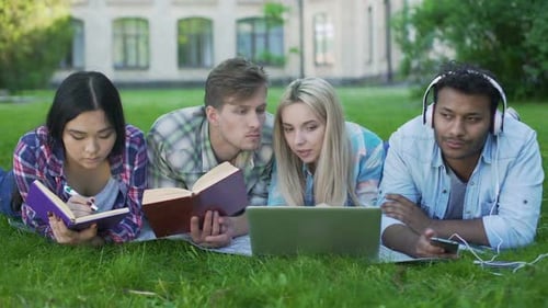 Gruppe von Freunden, die auf dem Campus auf dem Rasen liegen und sich auf den Test vorbereiten, Studentenleben