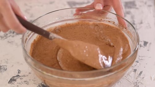 Hands Mixing Brown Cake Batter in Glass Bowl