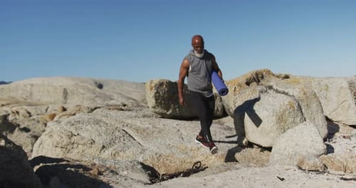 Senior african american man exercising walking on rocks by the sea