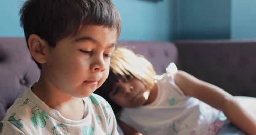 Brother and sister at home during Coronavirus lockdown, sitting on sofa, watching a movie.