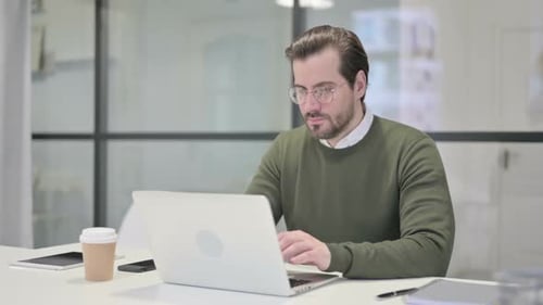 Young Businessman Showing Thumbs Up Sign While Using Laptop in Office