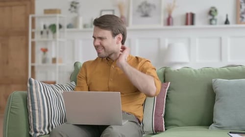 Man Rubs Neck with Laptop at Home