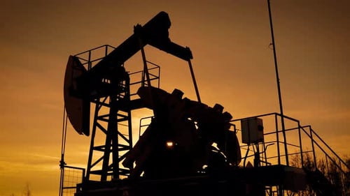 Der bewegende große Pumpjack pumpt bei Sonnenuntergang Erdöl vom Boden, Blick gegen den orangefarbenen Himmel