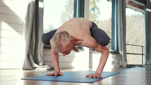 Mature Man Balances in Crow Yoga Pose Indoors