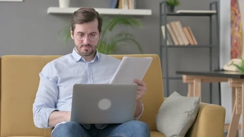 Man Working on Laptop with Documents at Home