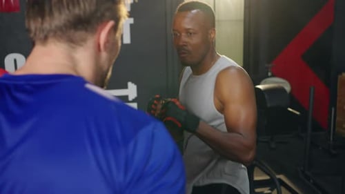 4K African man practicing boxing exercise with male sport trainer at gym.