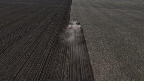 Tractor with harrow system plowing ground on cultivated farm field, agriculture.