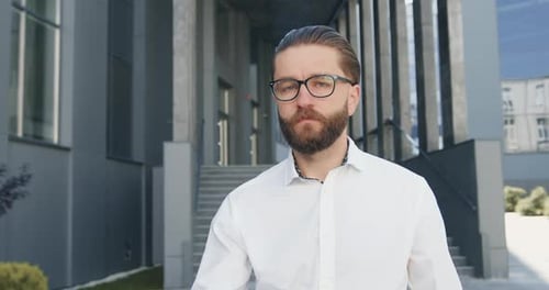 Businessman in Glasses which Poses on Camera on the Background of Urban modern Building