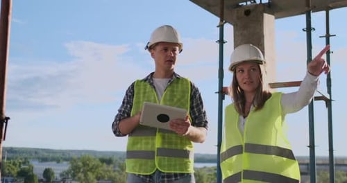 Professional Engineers in Safety Vests and Helmets Working with Digital Tablet and Blueprints