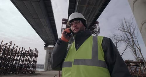 Construction Worker Talking on Phone Under Bridge