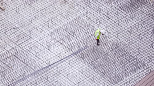 Construction Worker Inspecting Rebar Grid on Concrete Foundation