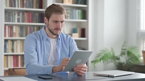 Man Reacting to Loss on Tablet While Sitting in Office