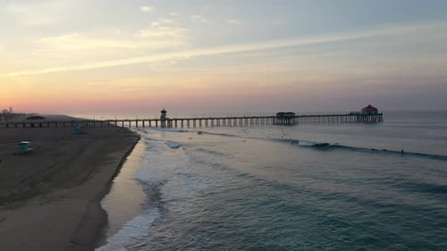 Stunning 4k view of the sunrise through the pier as surfers catch a wave in Surf City USA California