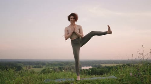 A Young Woman Does Yoga Exercises Standing on the Top of a Forest Mountain Against the Background of