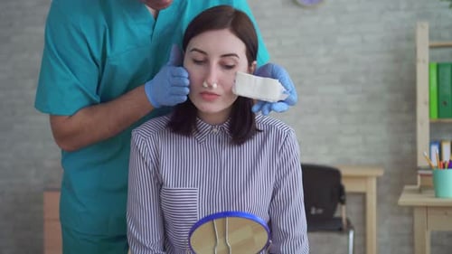 Doctor Removing Bandage From Woman's Nose
