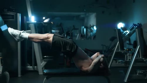 A Handsome Young Muscular Sportsman is Doing Exercise on a Fitness Machine in the Gym