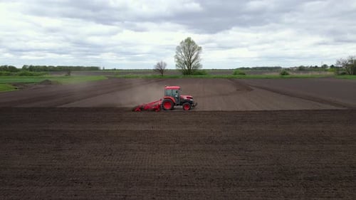 Slow Motion Aerial Shot of Tractor Plowing a Small Field with Blowing Dust in the Countryside of a