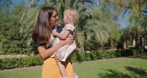 Beautiful Mother and Cute Little Daughter Talking in a Green Tropical Park