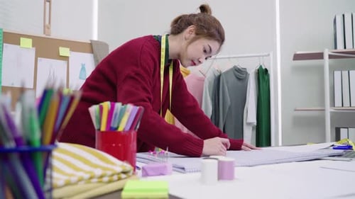 Young Asian woman fashion designer drawing using pencil and looking at paper in the workshop studio.