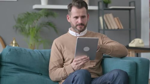 Man Uses Tablet and Celebrates on Couch