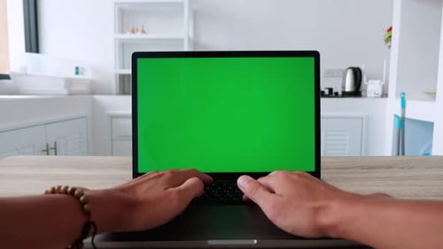 POV Shot of Man Sitting at Kitchen Table and Typing on the Keyboard on Laptop Computer with Green