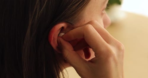 Woman Inserts Wireless Earbud While Holding Cellphone