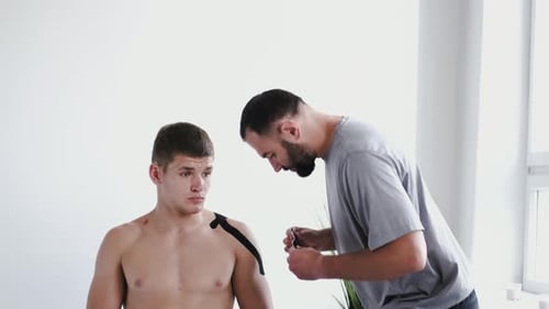 Osteopath Doing Kinesiology Taping on Patient's Shoulder in Clinic