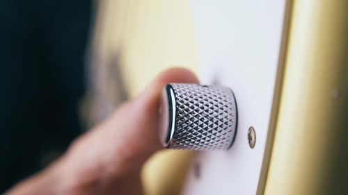 El dedo gira la perilla de control de volumen plateada del bajo